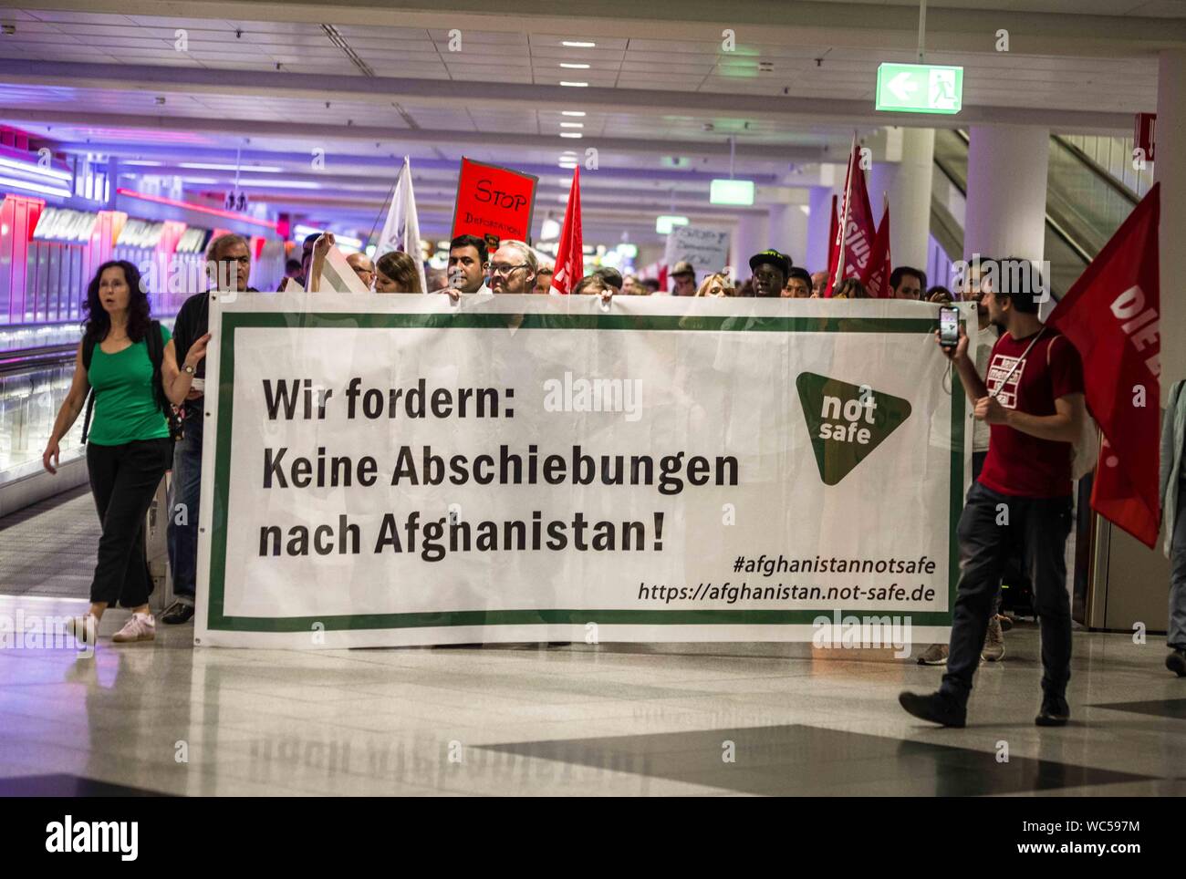 Monaco di Baviera, Germania. Il 27 agosto, 2019. ''Abbiamo domanda no deportazioni in Afghanistan''. In coincidenza con una deportazione di massa dalla Germania in Afghanistan, 100 rifugiati, i migranti e gli attivisti ha organizzato una manifestazione di protesta contro la Germania della politica dei rifugiati presso l' Aeroporto Internazionale di Monaco di Baviera. Tra le critiche includono l'uso di Ankerzentren (centri di ancoraggio) progettato per sequestrare i rifugiati e i migranti lontano dalla società, asilo sleale delle valutazioni effettuate dal BAMF, il Dublin III Convenzione e il controverso 'safe terra d origine'' determinazioni che sono stati utilizzati per accelerare le deportazioni in guerra Foto Stock