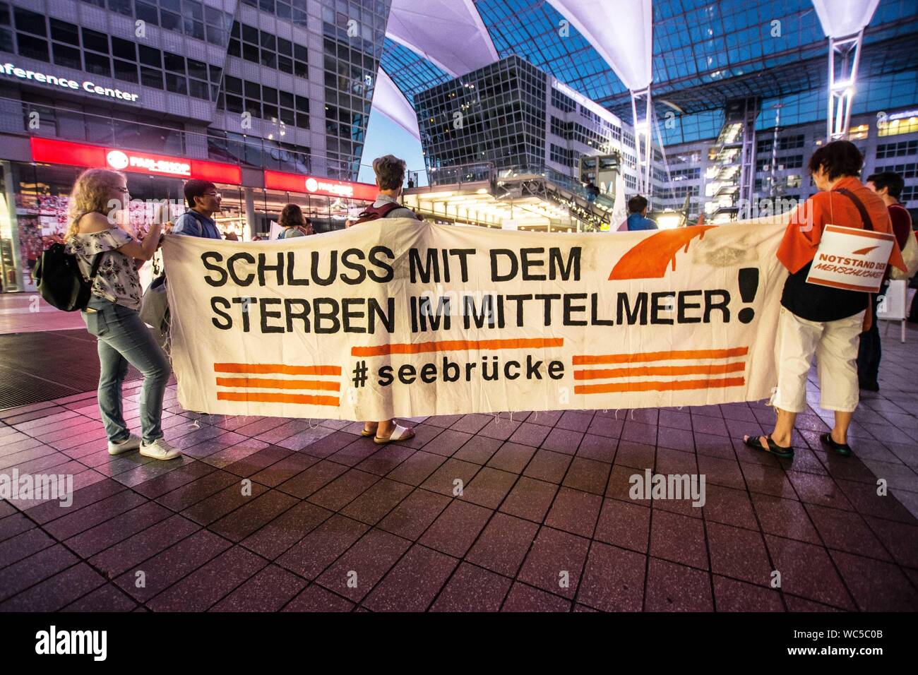 Monaco di Baviera, Germania. Il 27 agosto, 2019. ''Apertura delle frontiere per i rifugiati". In coincidenza con una deportazione di massa dalla Germania in Afghanistan, 100 rifugiati, i migranti e gli attivisti ha organizzato una manifestazione di protesta contro la Germania della politica dei rifugiati presso l' Aeroporto Internazionale di Monaco di Baviera. Tra le critiche includono l'uso di Ankerzentren (centri di ancoraggio) progettato per sequestrare i rifugiati e i migranti lontano dalla società, asilo sleale delle valutazioni effettuate dal BAMF, il Dublin III Convenzione e il controverso 'safe terra d origine'' determinazioni che sono stati utilizzati per accelerare le deportazioni in zone di guerra. (Credito Foto Stock