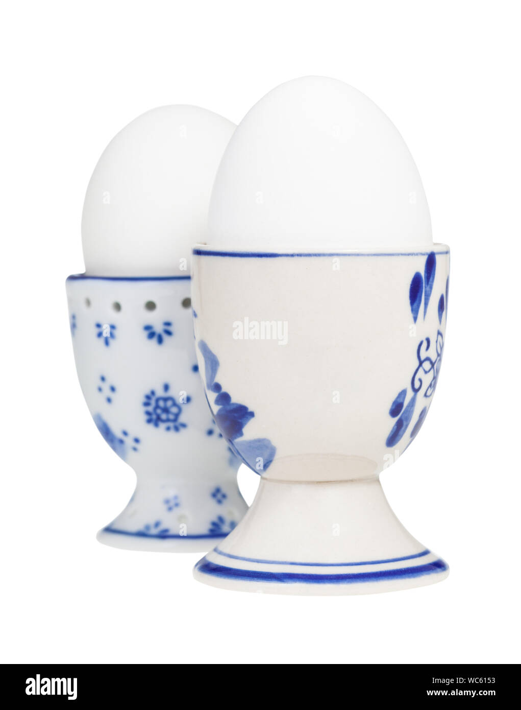 Vista laterale del bianco due uova sode in ceramica tazze uovo isolato su sfondo bianco, l'uovo con un'estremità smussata in primo piano Foto Stock