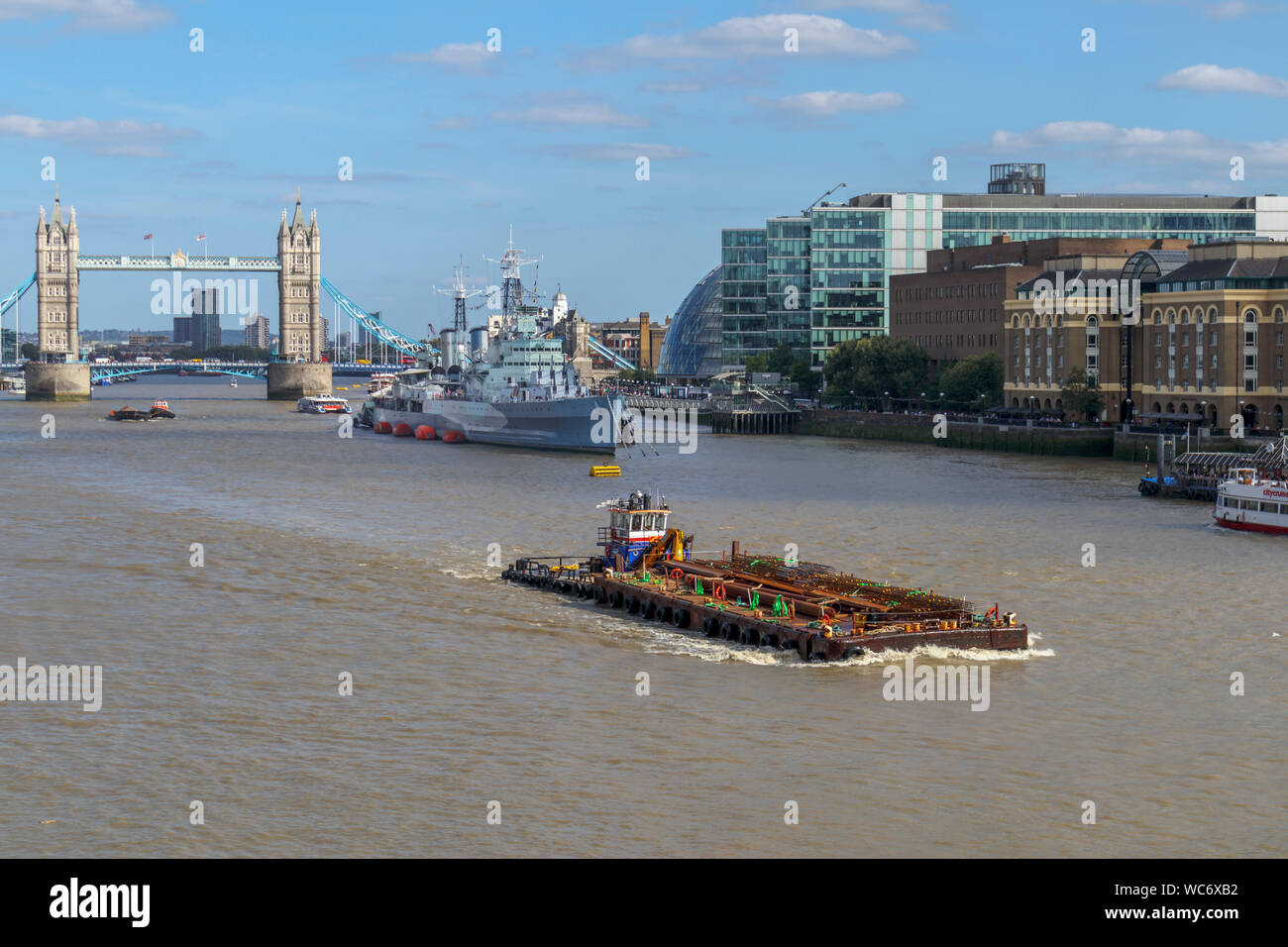 Una chiatta di grandi dimensioni nel pool di Londra sul Fiume Tamigi con una vista dell'iconico il Tower Bridge e HMS Belfast, visto dal London Bridge Foto Stock