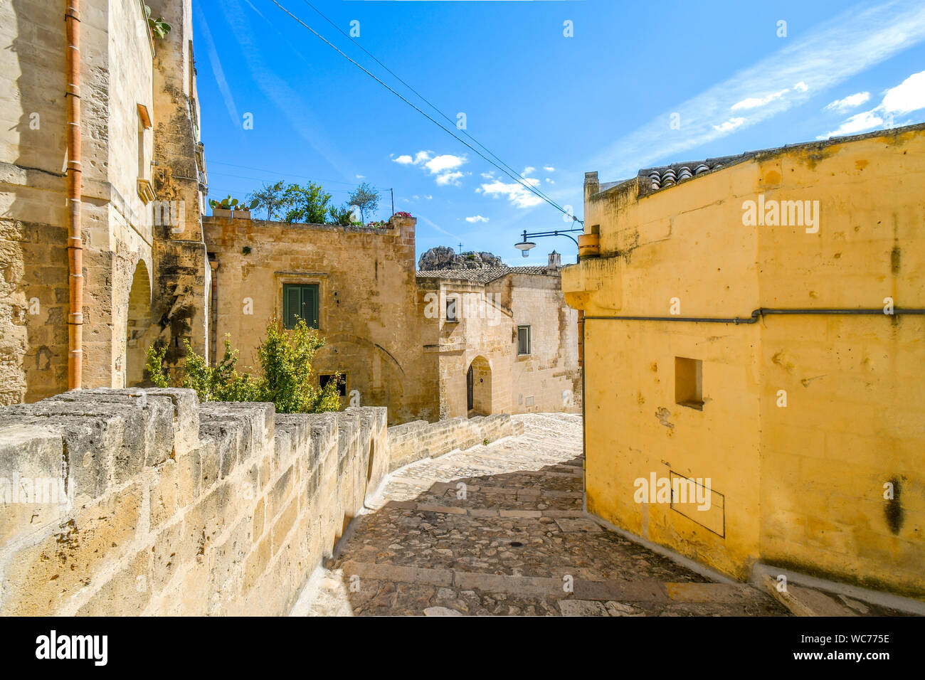 Una scala di pietra conduce verso il basso le case del passato e un dipinto luminosamente parete giallo in una zona residenziale della città antica di Matera, Italia. Foto Stock