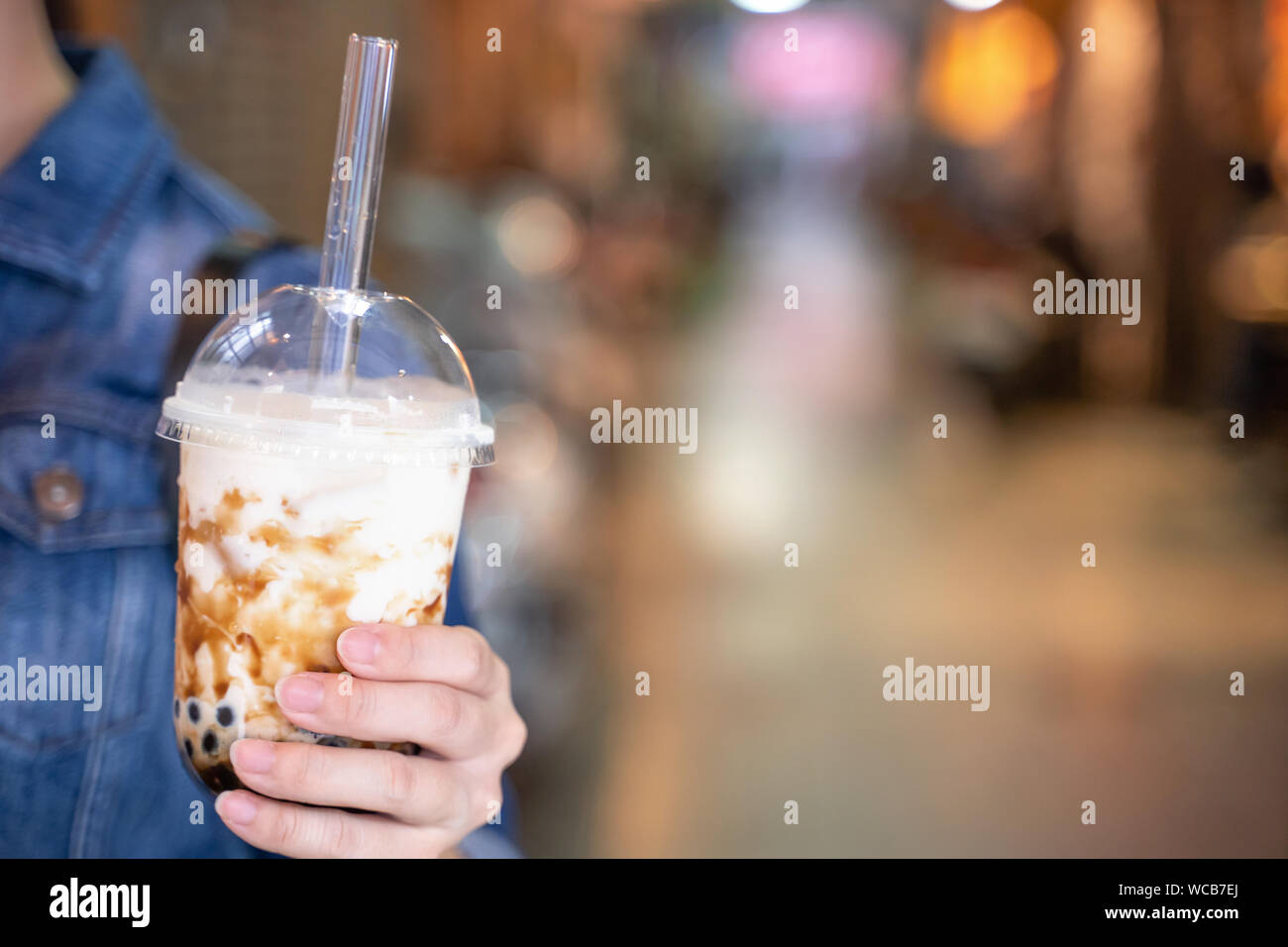 Ragazza giovane in camicia di denim è bere marrone zucchero aromatizzati tapioca pearl bubble latte tè con paglia di vetro nella notte di mercato di Taiwan, vicino bokeh di fondo Foto Stock