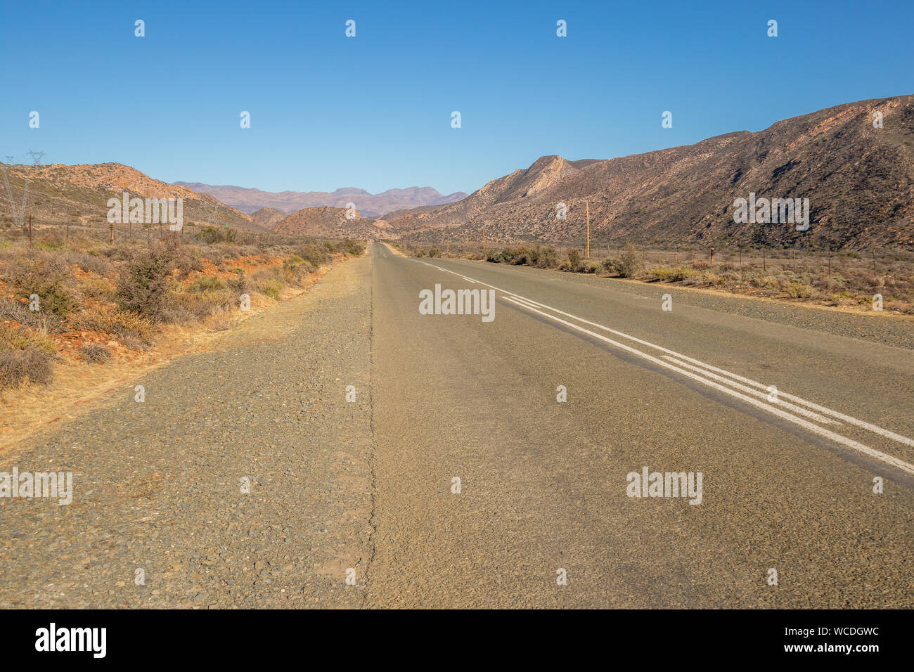 Un'autostrada conduce attraverso un paesaggio arido verso le colline all'orizzonte immagine con spazio copia in formato orizzontale Foto Stock