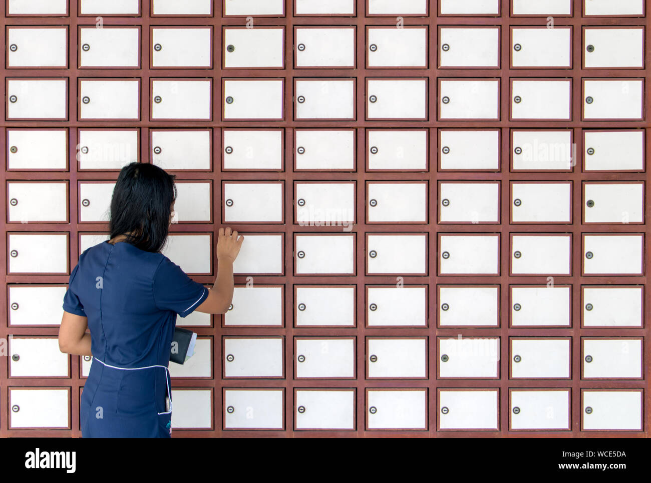 Una giovane donna si sblocca la cassetta postale sulla parete piena di caselle di posta. Donna che utilizza le cassette di deposito sulla parete. Foto Stock