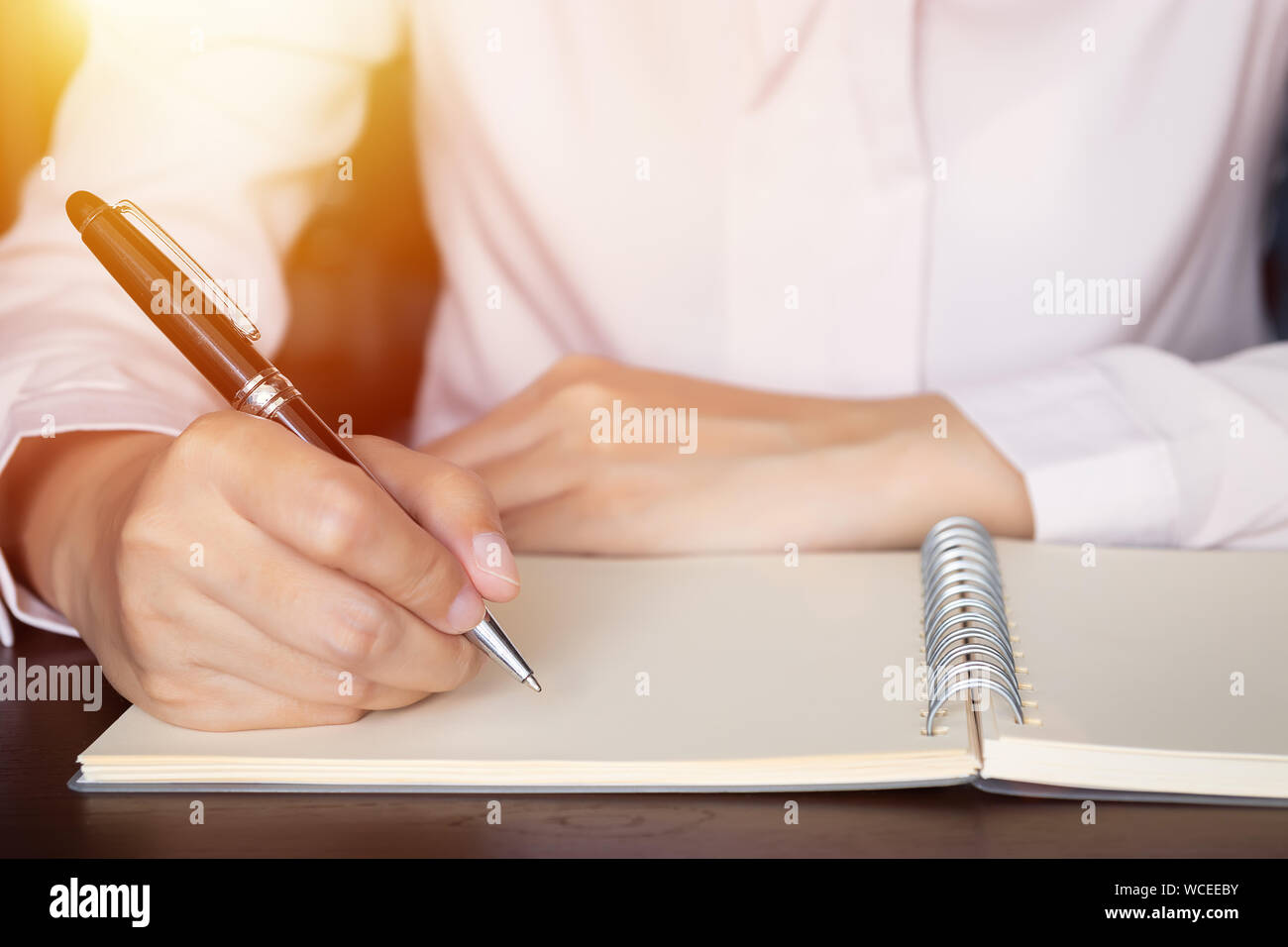 Close up di business donna mani la scrittura nel blocco note a spirale sul tavolo di legno Foto Stock