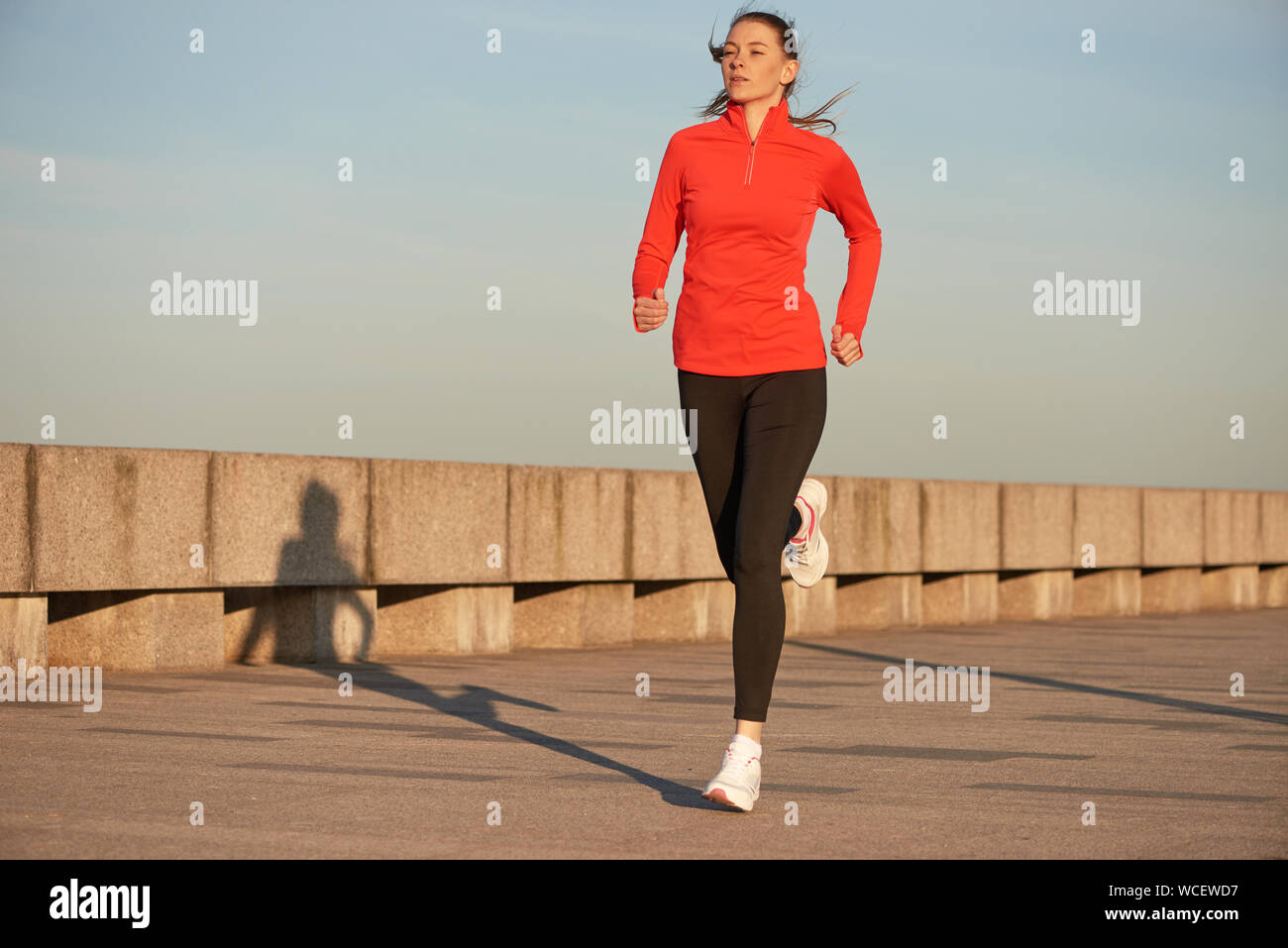 Una donna per fare jogging in rosso acceso camicia e leggins nero sulla  strada a sunrise. In esecuzione su calcestruzzo quay Foto stock - Alamy