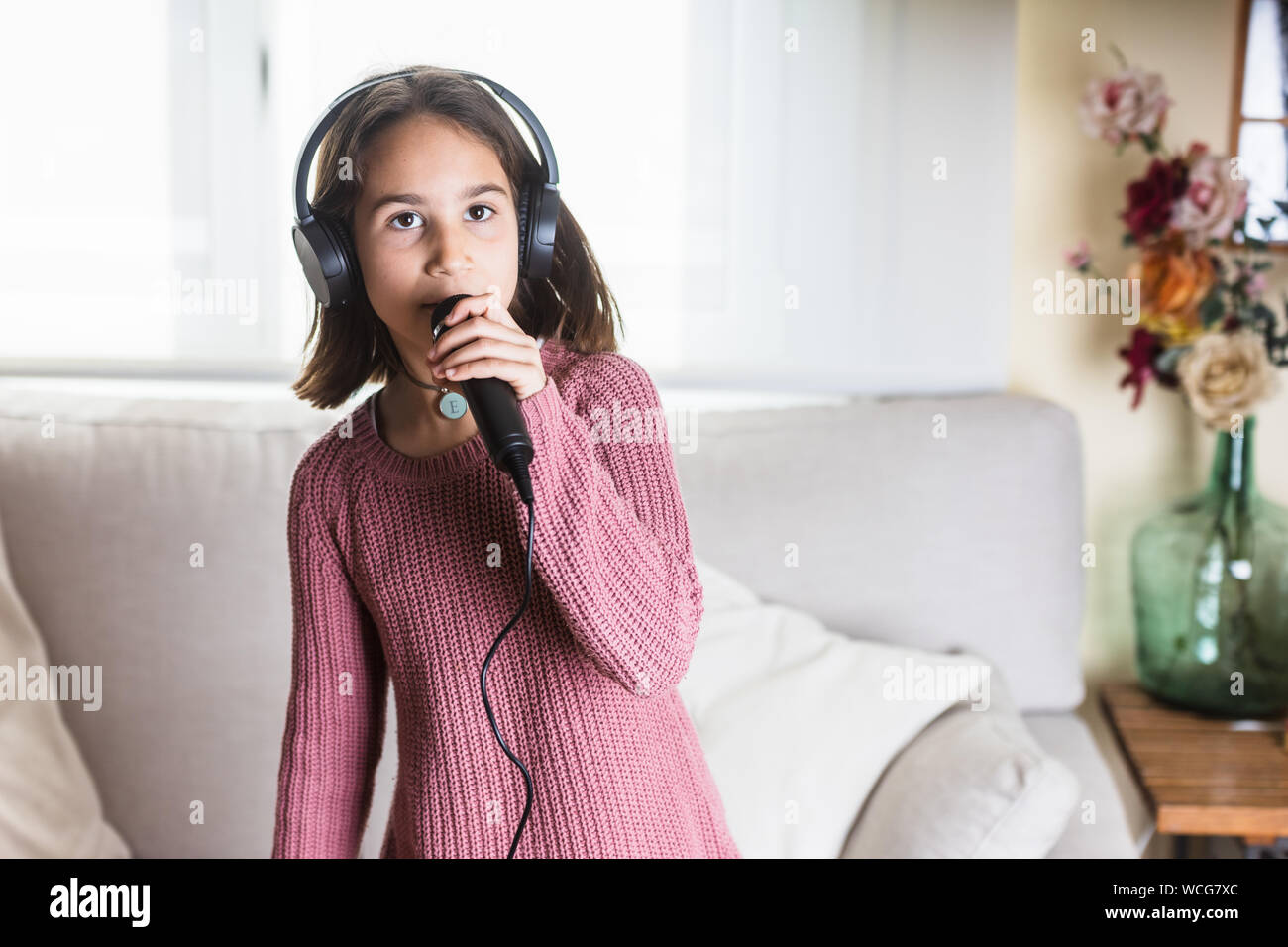 Niña cantando feliz con auriculares y micrófono en interior de casa Foto Stock