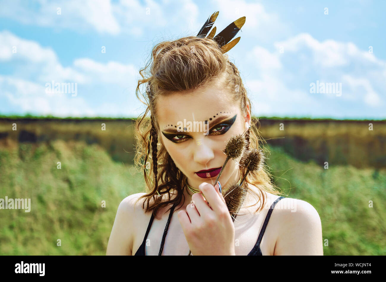 Ritratto di una ragazza aggressiva con specchio amazon viking presse fiori coccolone thistle per il suo volto. Foto Stock