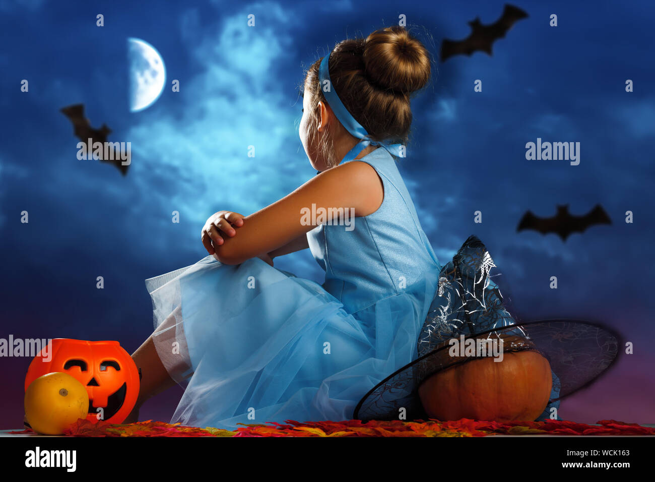 Festa di Halloween. Una bambina vestita come la principessa Cenerentola si siede con la schiena circondato da zucche e guarda alla sera il cielo illuminato dalla luna. Foto Stock
