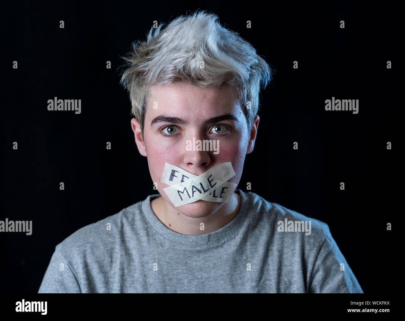 Transgender teenager con la bocca chiusa a tenuta su nastro con parole maschio e femmina scritto in tabù sociale delle diversità di genere concetto. Trans ragazzo non in grado di c Foto Stock