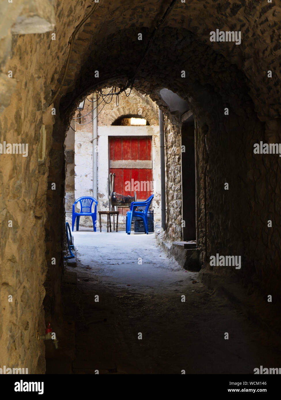 Stretto vicolo nel borgo medievale di Mesta a Chios Island, Grecia. Tabella blu e sedie di plastica. Foto Stock