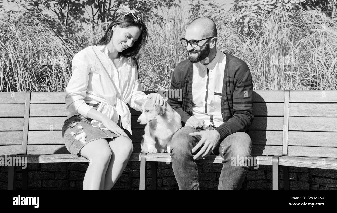 La felice coppia sono seduti sulla panchina del parco con un piccolo cane. Carino corgi Pembroke cucciolo sulle sue mani dei proprietari. Corgi cucciolo è seduto in pa Foto Stock