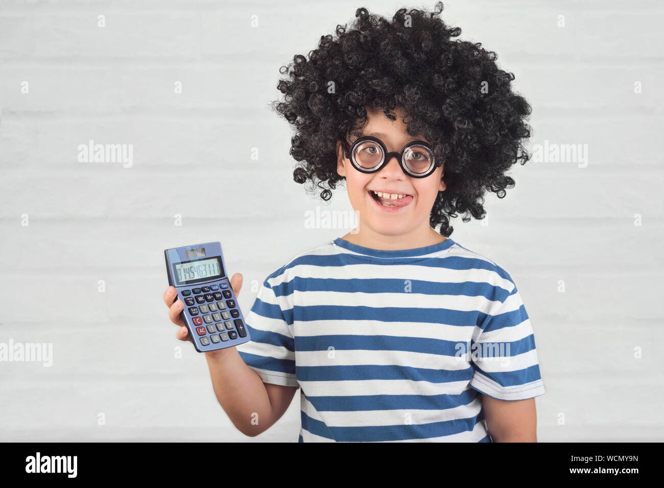 Funny bambino con la calcolatrice indossando occhiali nerd su Sfondo mattone Foto Stock