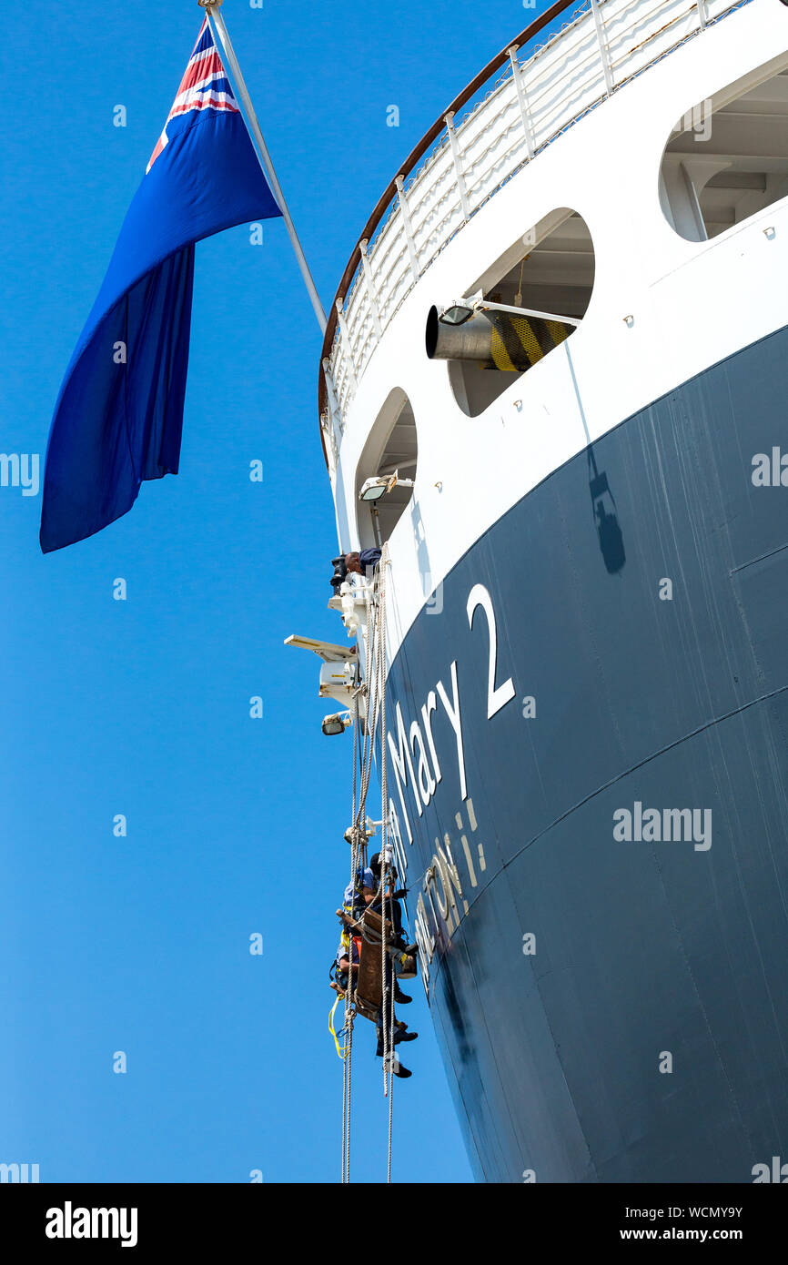 I membri dell'equipaggio pittura Queen Mary 2 , Nome della nave sulla poppa della nave mentre al fianco di Liverpool docks. Inghilterra, Regno Unito Foto Stock