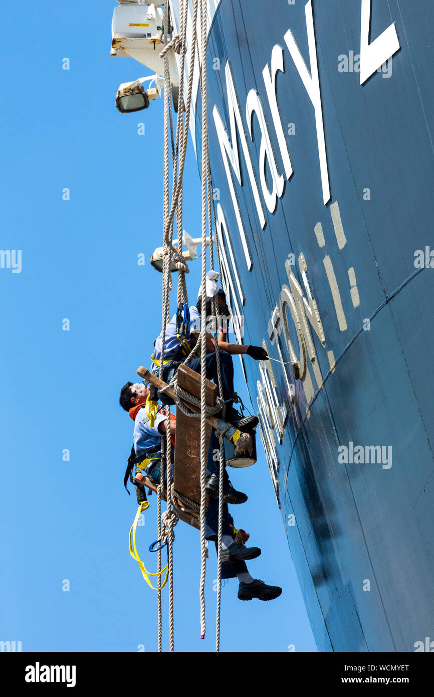 I membri dell'equipaggio pittura Queen Mary 2 , Nome della nave sulla poppa della nave mentre al fianco di Liverpool docks. Inghilterra, Regno Unito Foto Stock