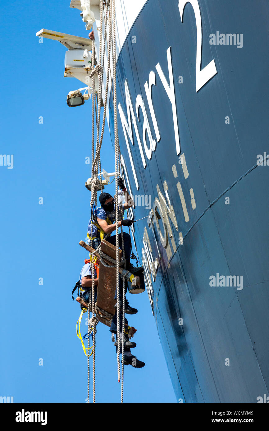 I membri dell'equipaggio pittura Queen Mary 2 , Nome della nave sulla poppa della nave mentre al fianco di Liverpool docks. Inghilterra, Regno Unito Foto Stock