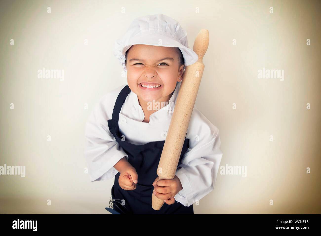Ritratto di ragazza sorridente In Chef bianchi Azienda Mattarello contro la parete Foto Stock