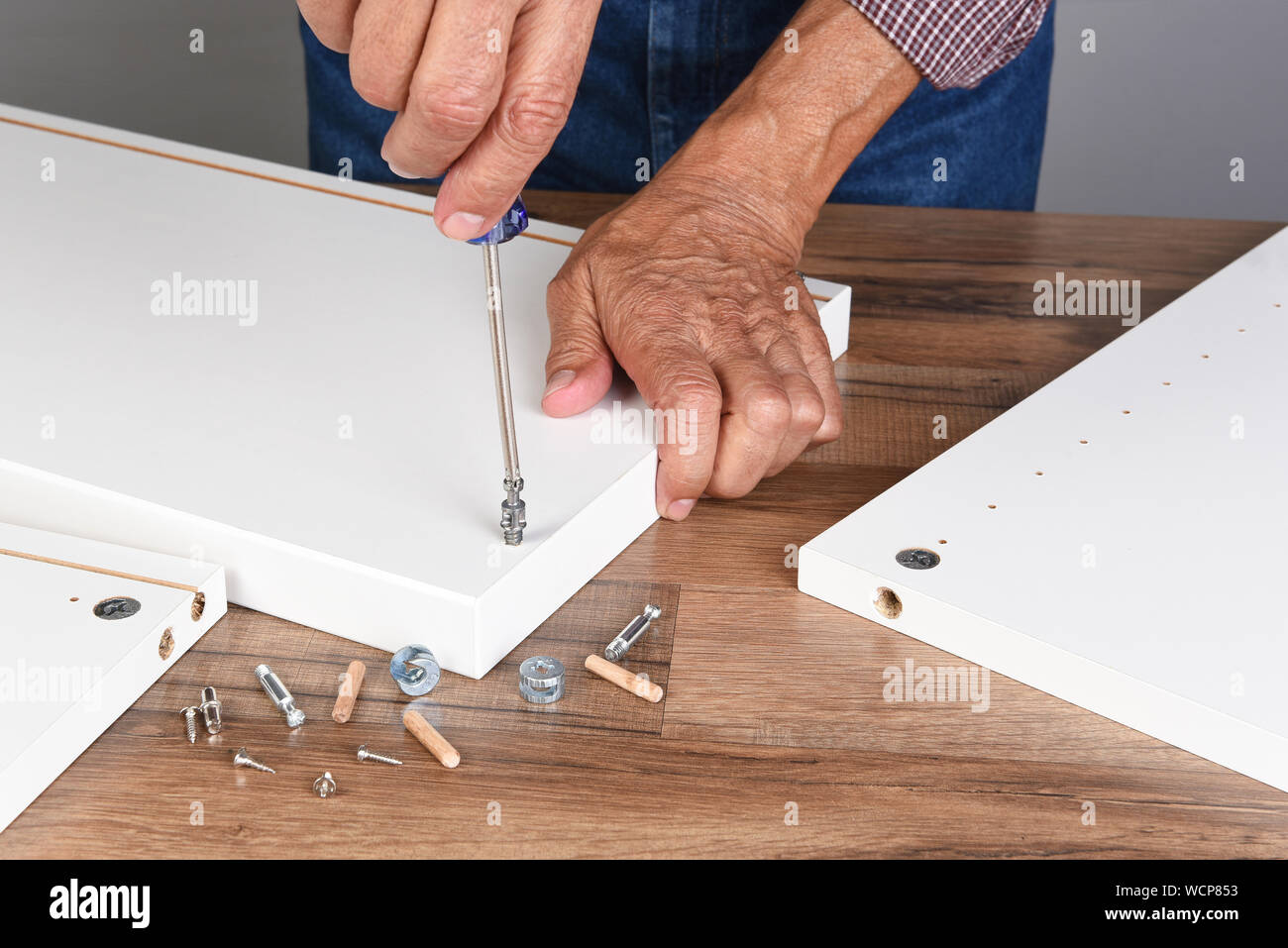 Un uomo di assemblaggio di un pezzo di DIY di mobili. La persona che sta utilizzando un cacciavite per montare un pezzo di hardware. Foto Stock