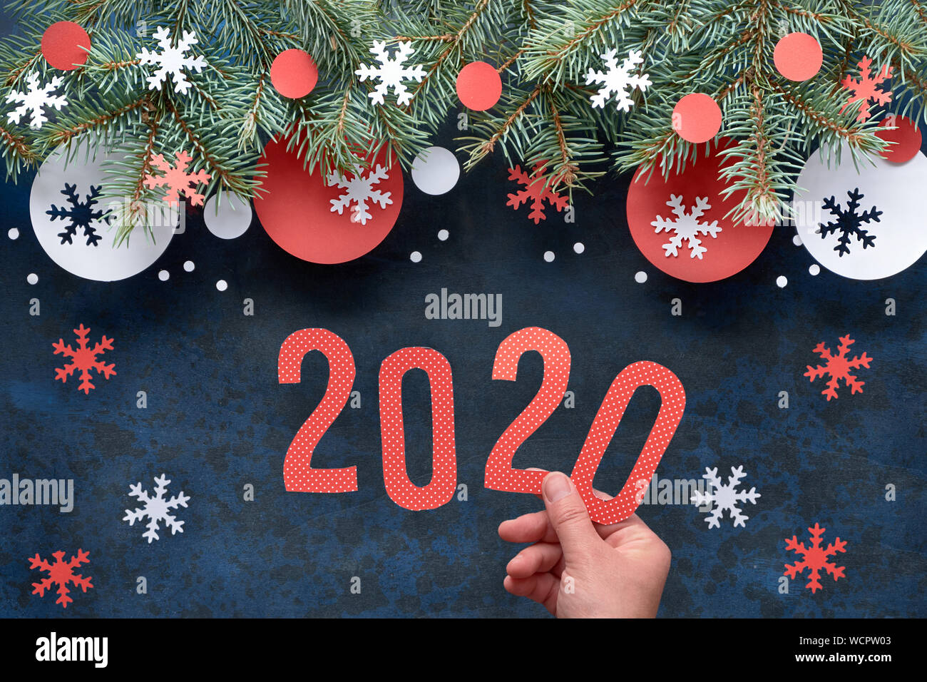 Mano azienda numero 2020, Natale sfondo con ramoscelli di abete rosso e bianco decorazioni di carta. Appartamento laico, vista dall'alto sulla astratta scuro dello sfondo. Foto Stock