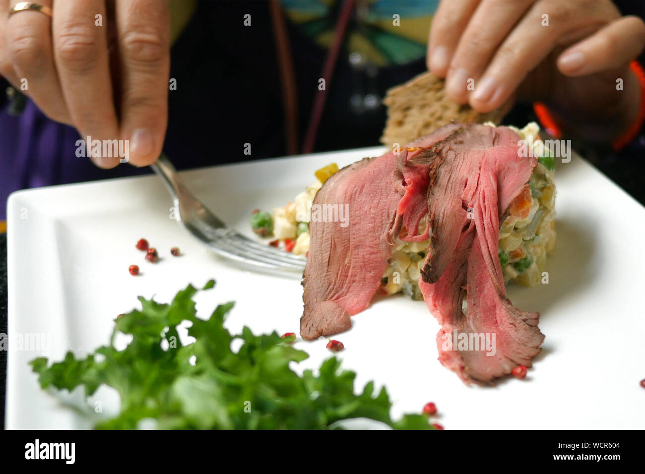 Una gustosa cena. Uomo di mangiare insalate tradizionali per i popoli slavi Olivier o insalata di verdure e carne in bar o un ristorante dalla piastra bianca. Sele Foto Stock