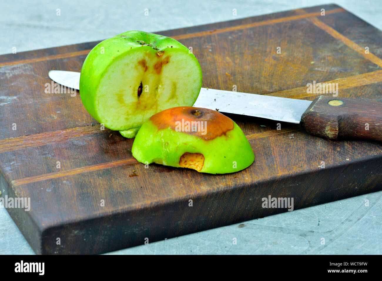 Mela tagliata aperta con un marcio area sul tagliere di legno con il coltello Foto Stock