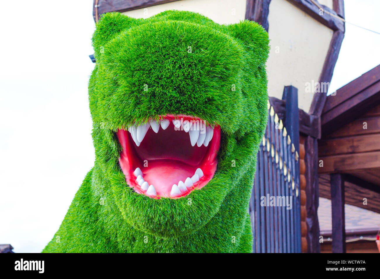 Dinosauro realizzato in erba artificiale. La bocca del dinosauro è aperta in modo tale che i denti taglienti e una linguetta rosa sono visibili. Foto Stock