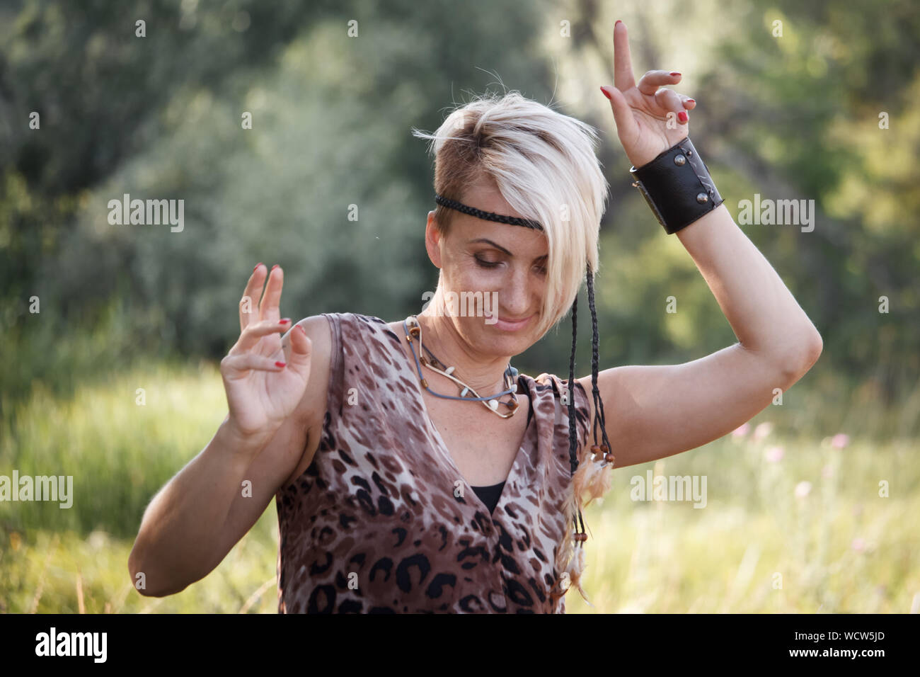 Close up donna adulta bionda danze e gode di vita su uno sfondo di prato erboso, il fuoco selettivo Foto Stock