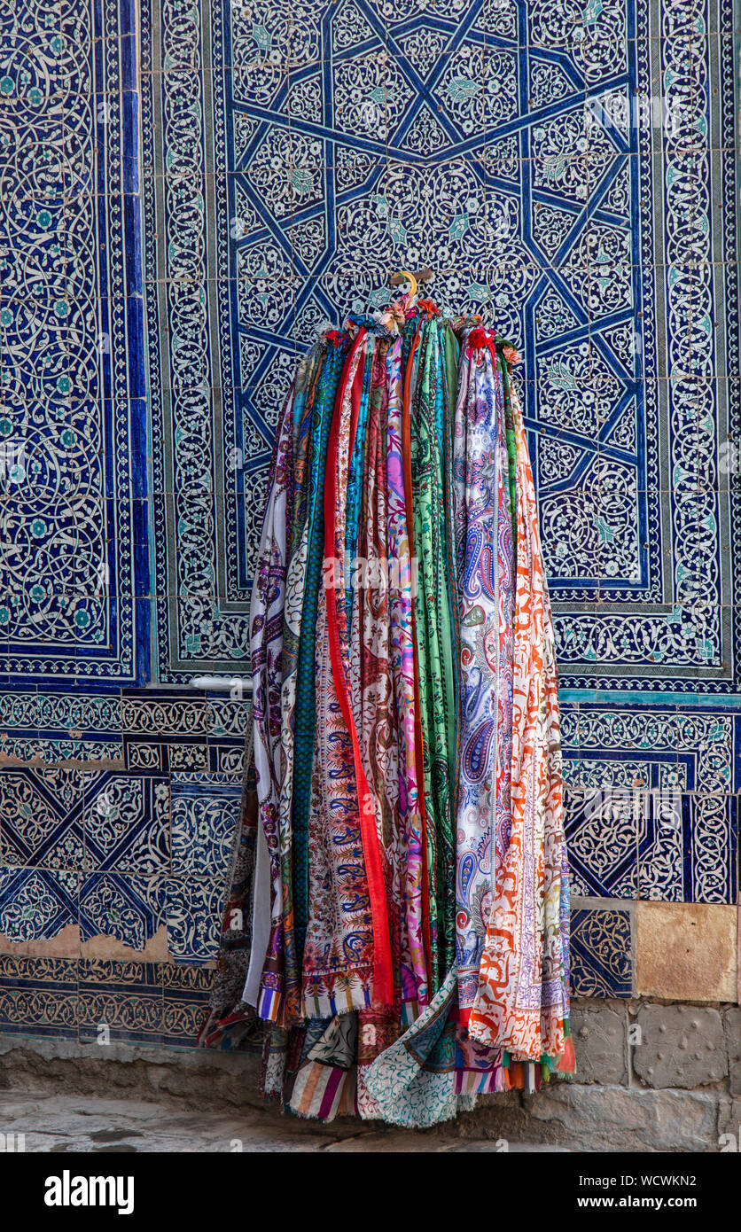 Tradizionali sciarpe colorate nella parte anteriore del tradizionale blu mosaico pareti piastrellate in una moschea nella città di Khiva in Uzbekistan. Foto Stock
