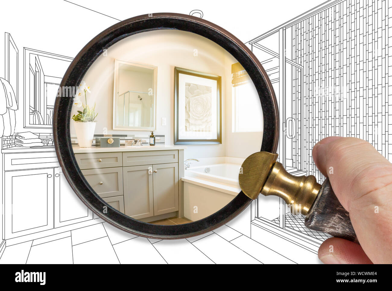 Mano che tiene la lente di ingrandimento rivelando bagno finito di costruire su disegno. Foto Stock