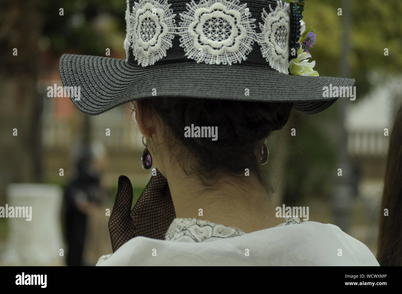 Giovane donna che indossa abiti modernista, con la sua mano sulla bocca. Indossa un grande cappello con fiori e guanti in rete. Eleganti donna che indossa abiti vintage Foto Stock