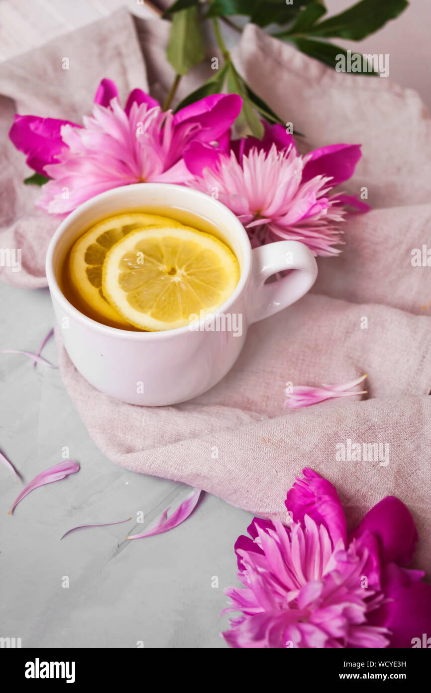 Vista di calda tazza di tè con un fresco e fette di limone e vibranti fiori rosa su sfondo bianco. Foto Stock