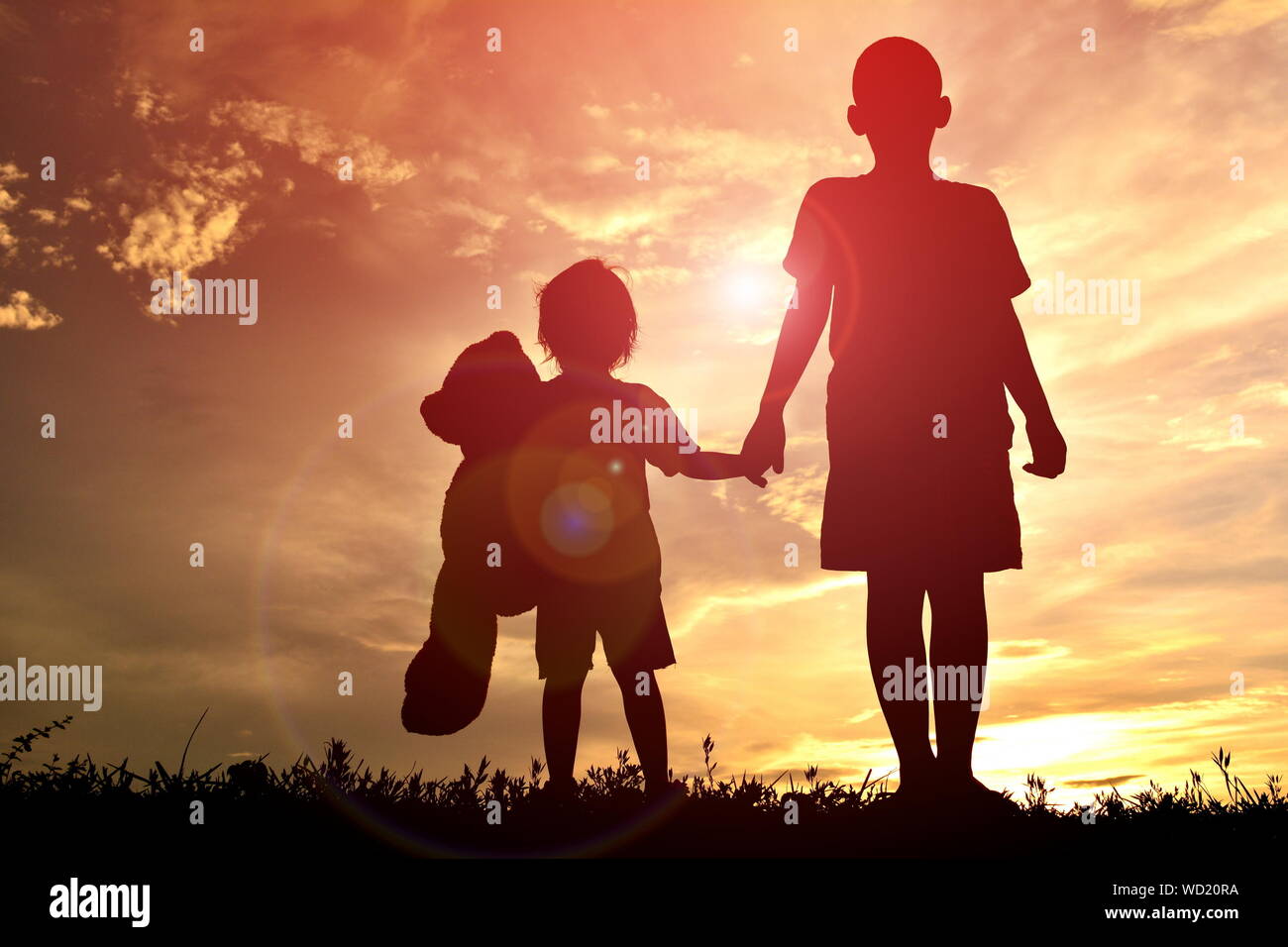 Basso angolo vista di Silhouette bambini tenendo le mani mentre in piedi contro il cielo durante il tramonto Foto Stock