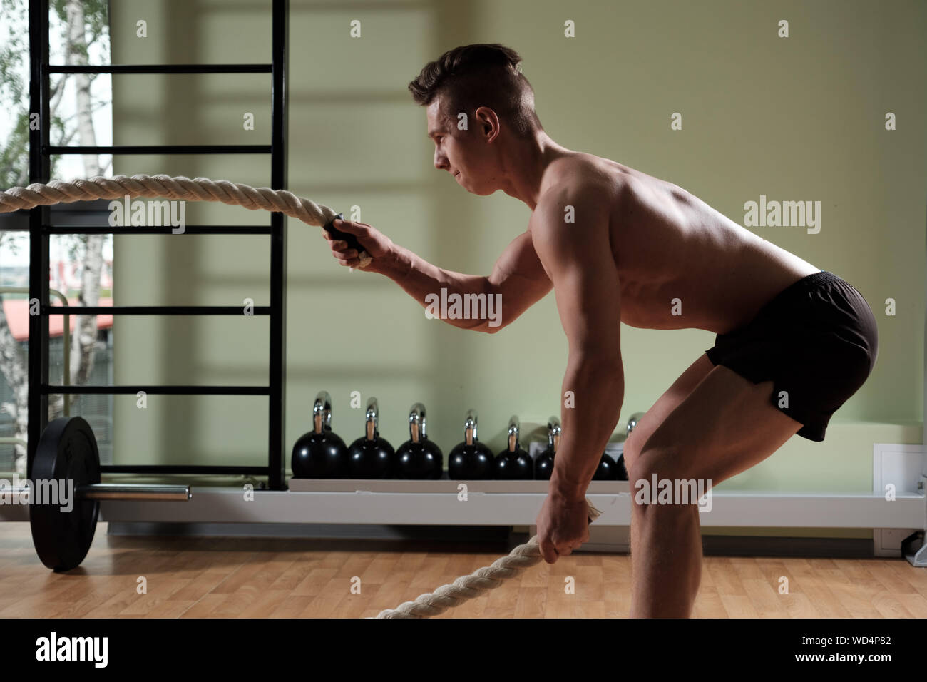 Uomo muscolare con corda di battaglia facendo esercizio di allenamento funzionale palestra. Vista di profilo. Foto Stock