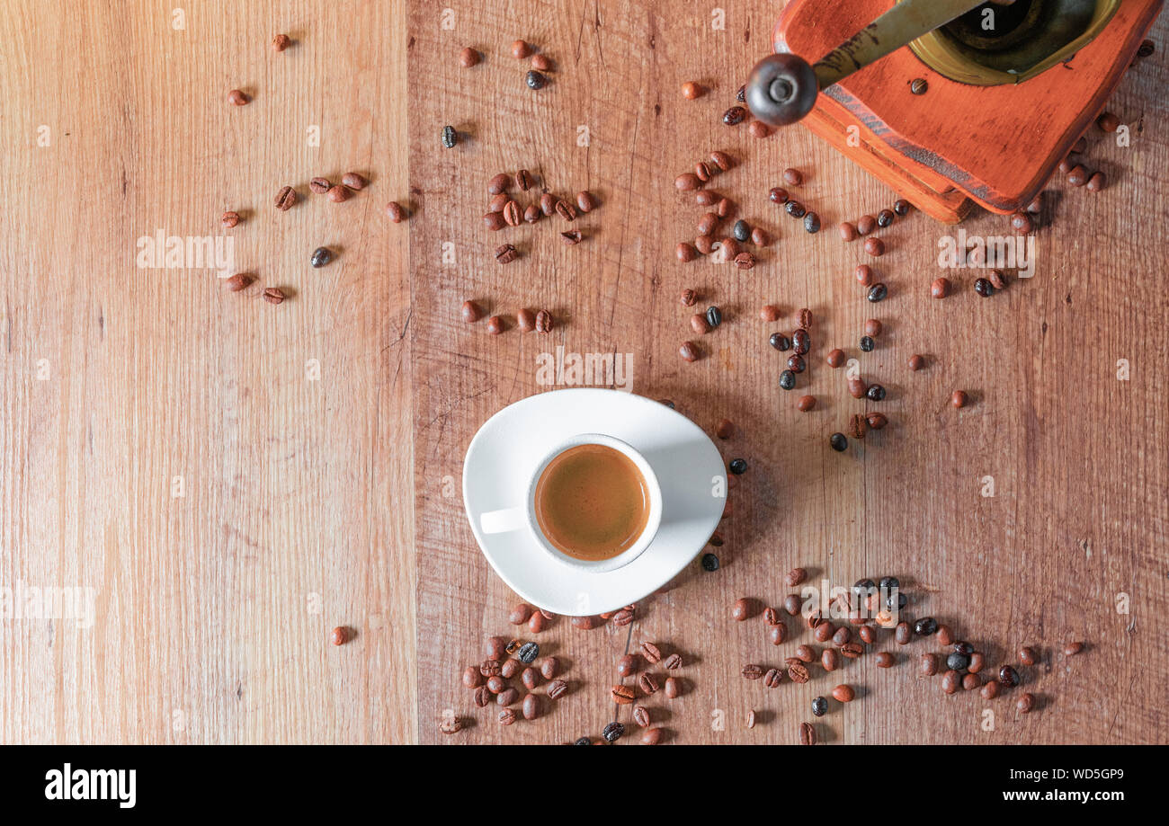 Vista dall'alto di un espresso servito in una tazza bianca circondata da chicchi di caffè tostati e un piccolo mulino su un tavolo di legno. Foto Stock