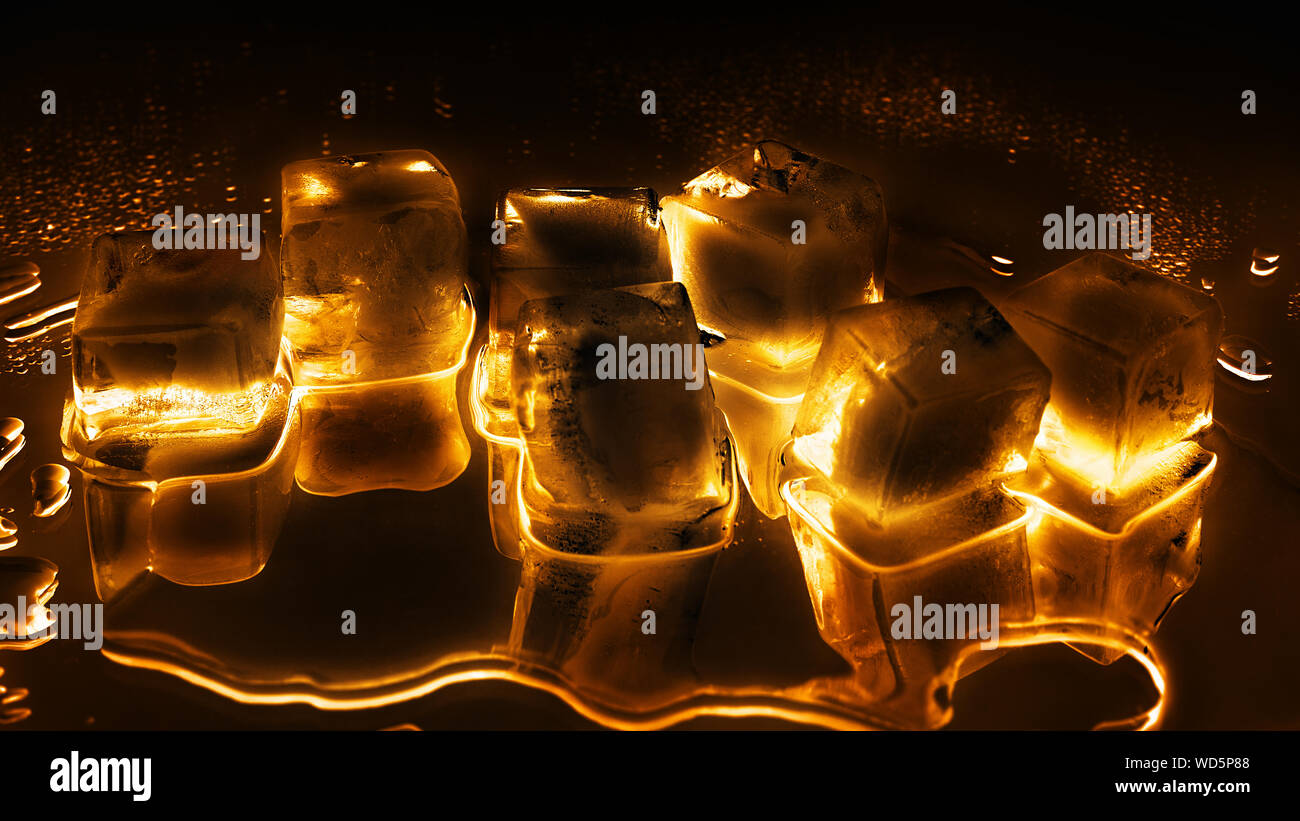 Golden cubetti di ghiaccio su sfondo nero closeup congelati trasparente ghiaccio fondente acqua lucida gocce di colore giallo brillante di luce di riflessione a specchio, abstract bevanda fredda Foto Stock