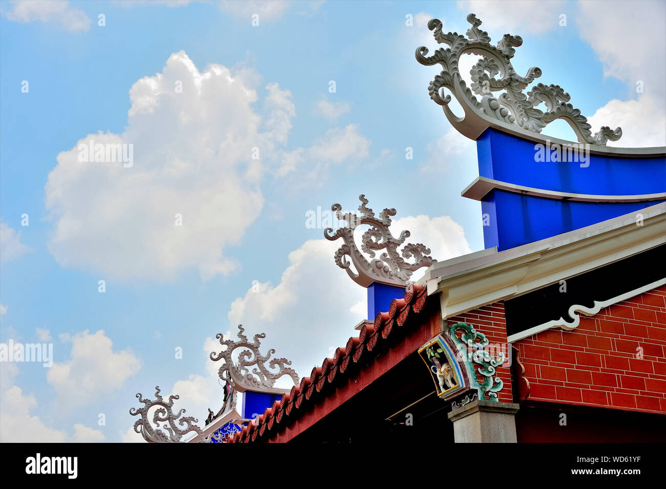 Il tetto del tempio cinese di Singapore con sculture in pietra forte e il design architettonico contro il cielo blu con nuvole Foto Stock