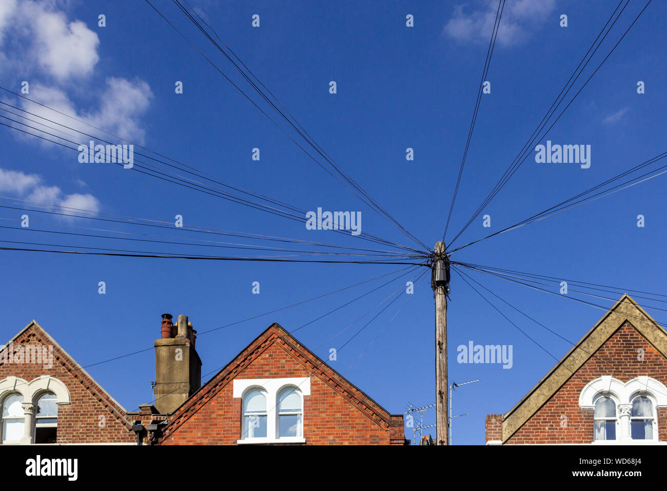 Cerca fino a cavi ad un palo telefonico di fronte dei tetti della scatola vittoriana ed un cielo blu Foto Stock