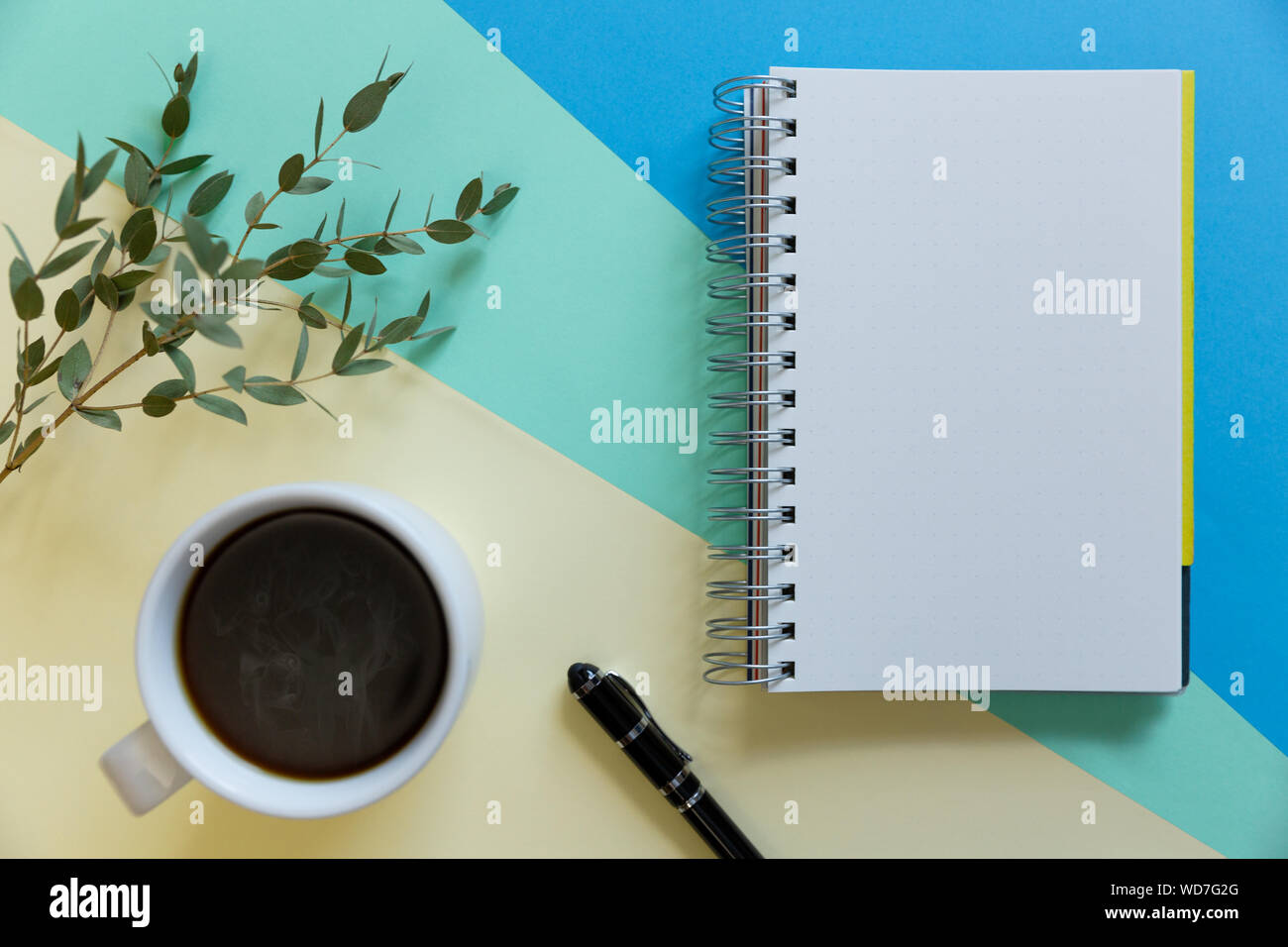 Blank notebook, caffè, ramo di eucalipto e penna su carta pastello sfondo. Business start-up e torna al concetto di scuole Foto Stock