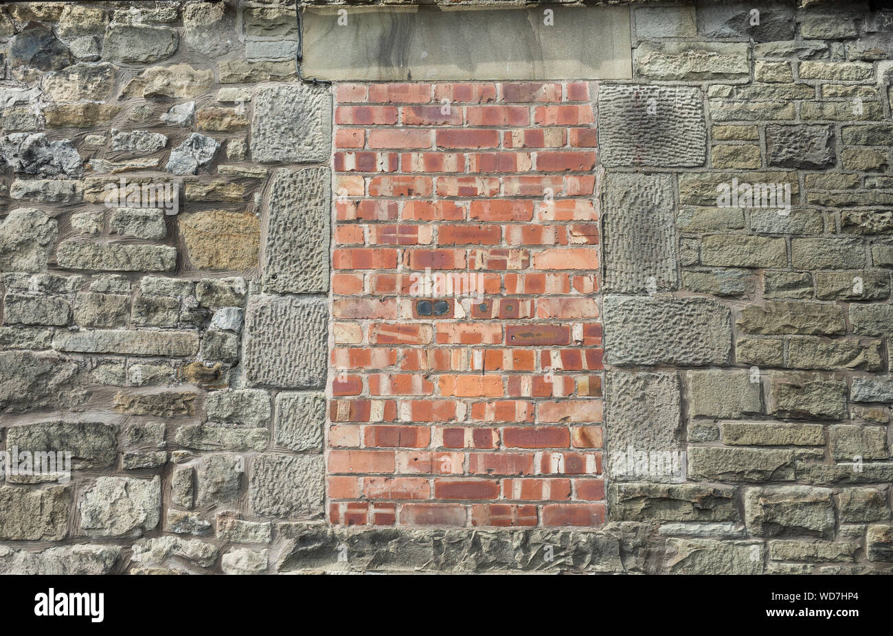 Un vecchio telaio di finestra in un muro di pietra, bloccati con mattoni rossi. Foto Stock