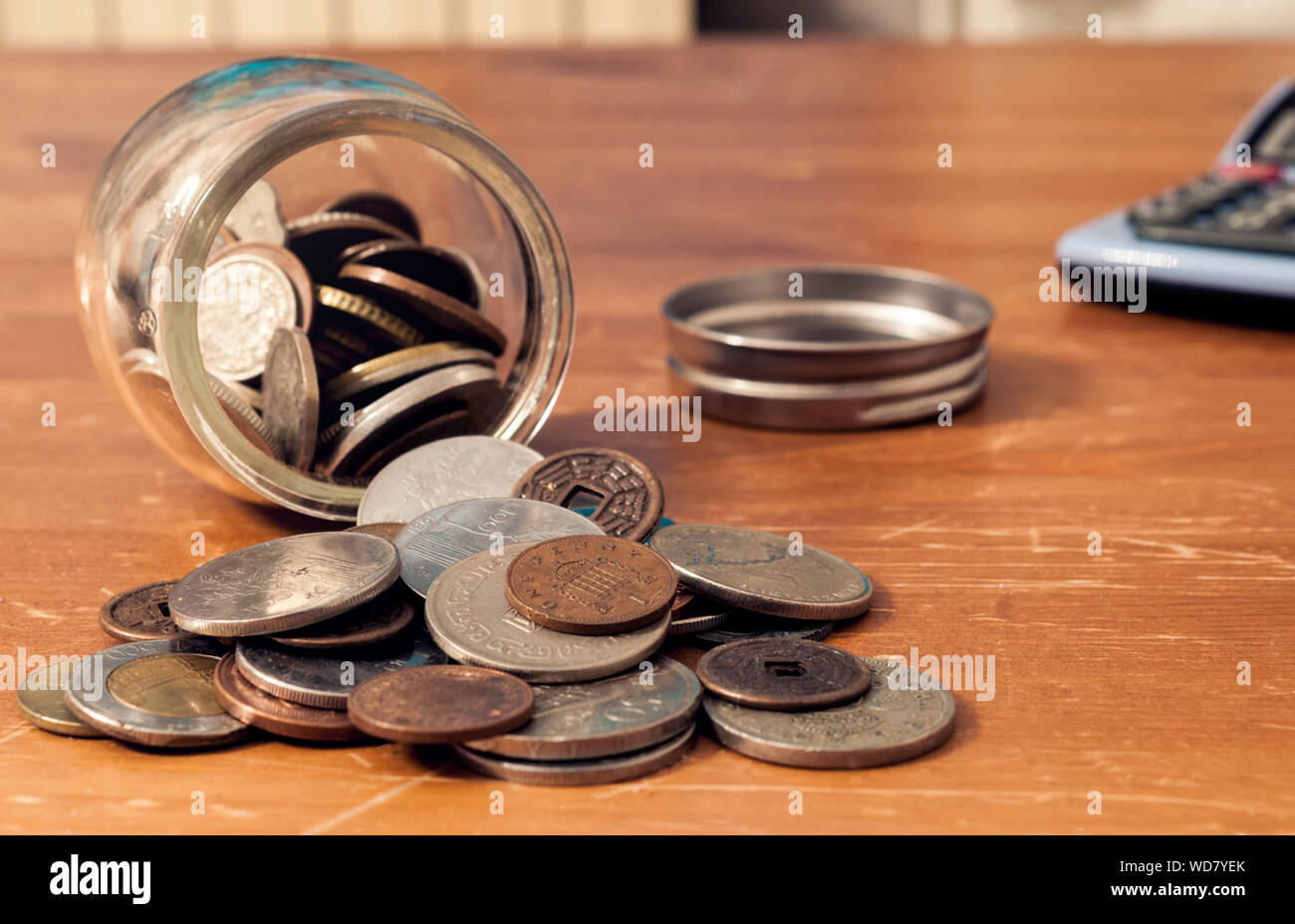 Coin jar capovolta sul tavolo con cappuccio e Calcolatrice in background. Questa immagine può essere utilizzata per rappresentare diversi concetti relativi al denaro. Foto Stock