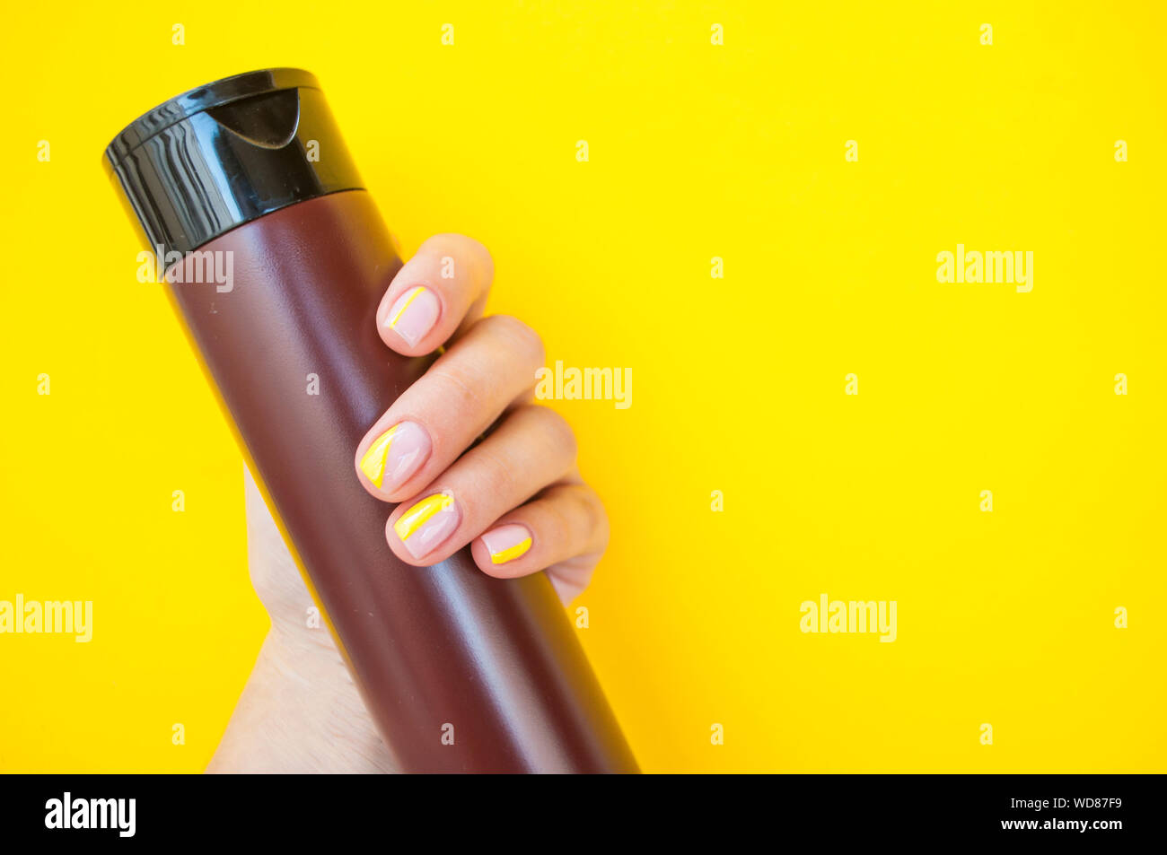 Giovane donna la mano con una bella manicure su giallo colore di sfondo tenendo in plastica bottiglia di cosmetici. Foto Stock