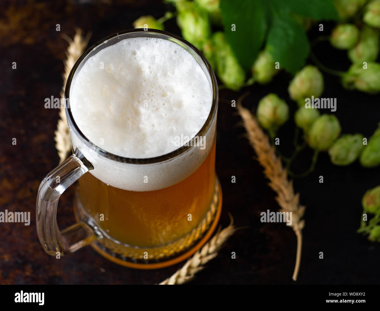 Una tazza di frumento non filtrata una birra su di un tavolo di legno verde con il luppolo e spighe di grano Foto Stock