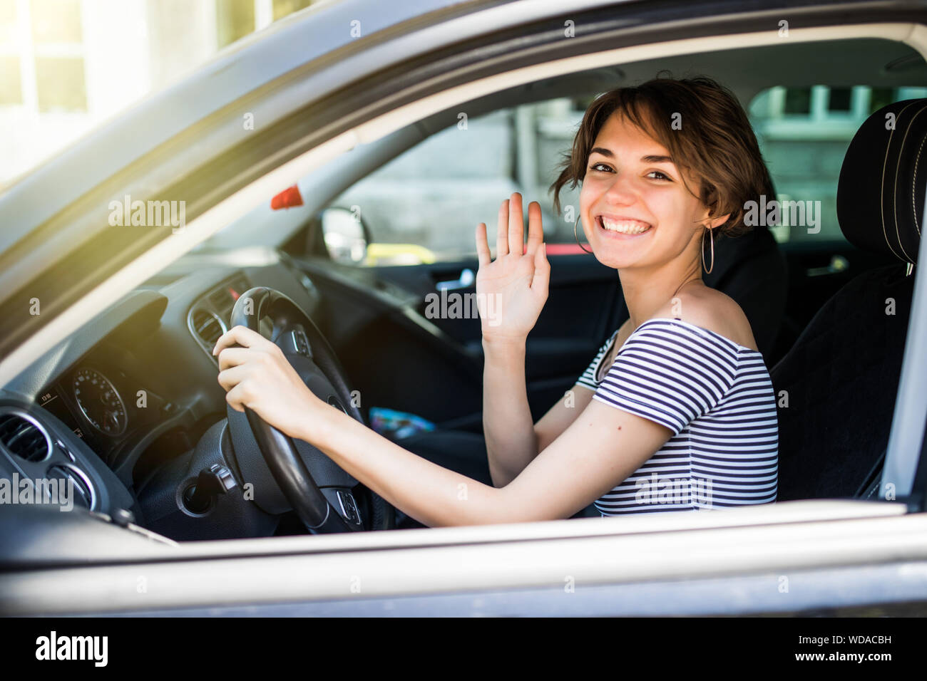 Bella giovane allegro donne guardando la fotocamera con il sorriso e sventolare mentre è seduto nella sua auto Foto Stock