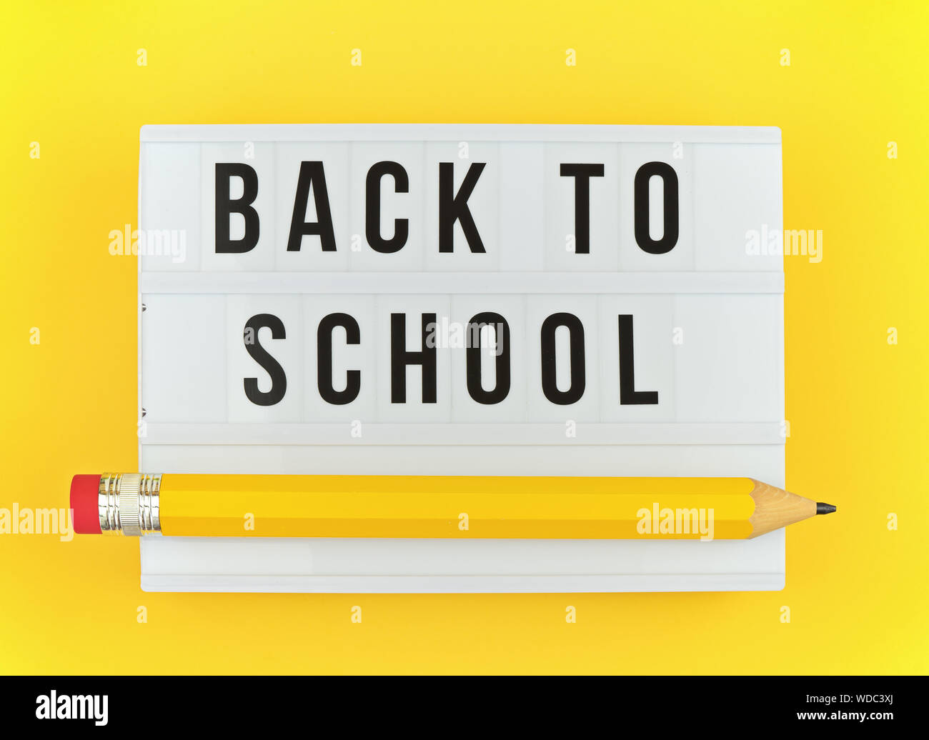 Lightbox con ritorno a scuola e testo grande divertente penna su sfondo giallo. Concetto di inizio della scuola e la vita degli studenti Foto Stock