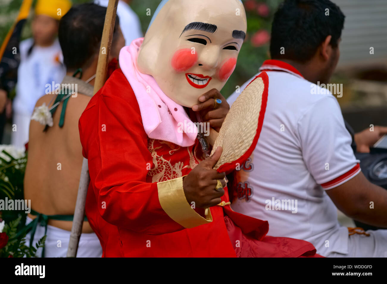 Una processione durante il Festival vegetariano di Phuket, in Thailandia, con un uomo che indossa una maschera cinese sorridente che cavalca una moto Foto Stock
