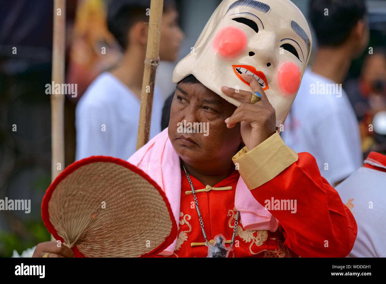 Una processione durante il Festival vegetariano di Phuket, in Thailandia, con un uomo che solleva la sua maschera cinese sorridente per rivelare il suo volto cupo sotto Foto Stock