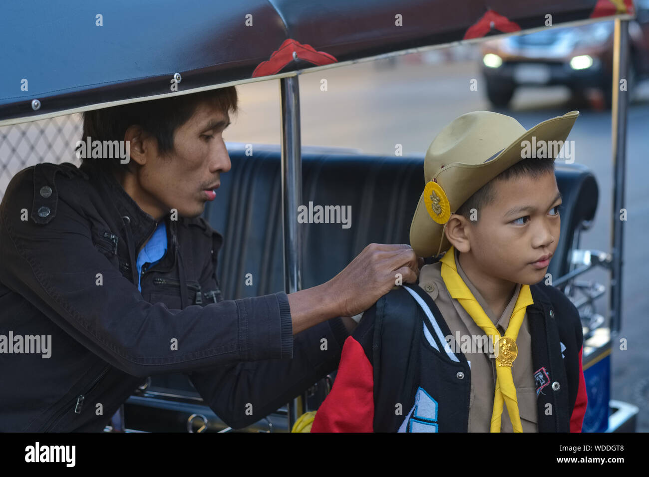 Un tuk-tuk driver in Bangkok, Thailandia, dispone i boy scout uniforme di suo figlio Foto Stock