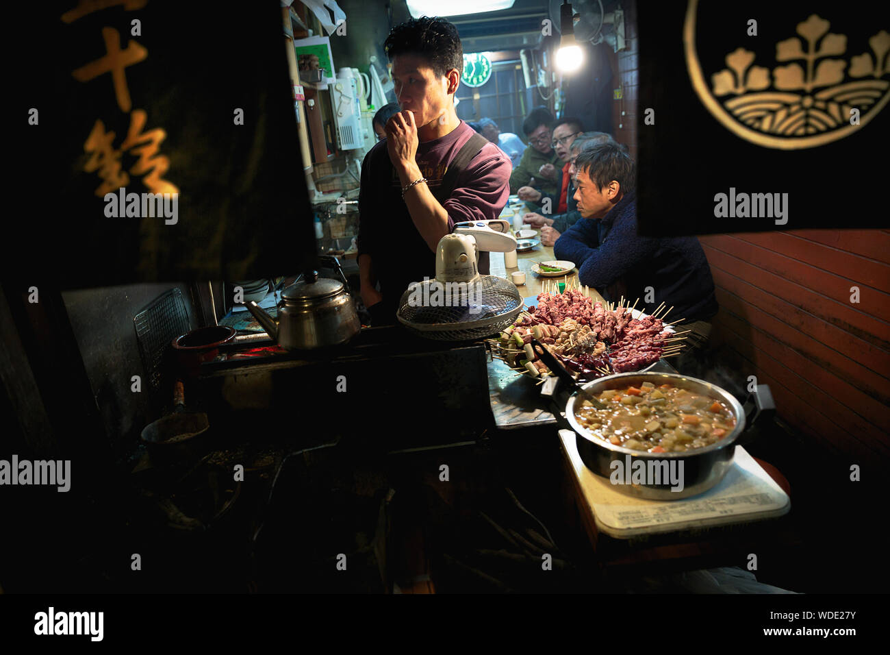 Le persone in attesa di mangiare grigliate di spiedini di pollo, carne di maiale e di carni bovine in un piccolo negozio a Omoide Yokocho vicolo. Foto Stock