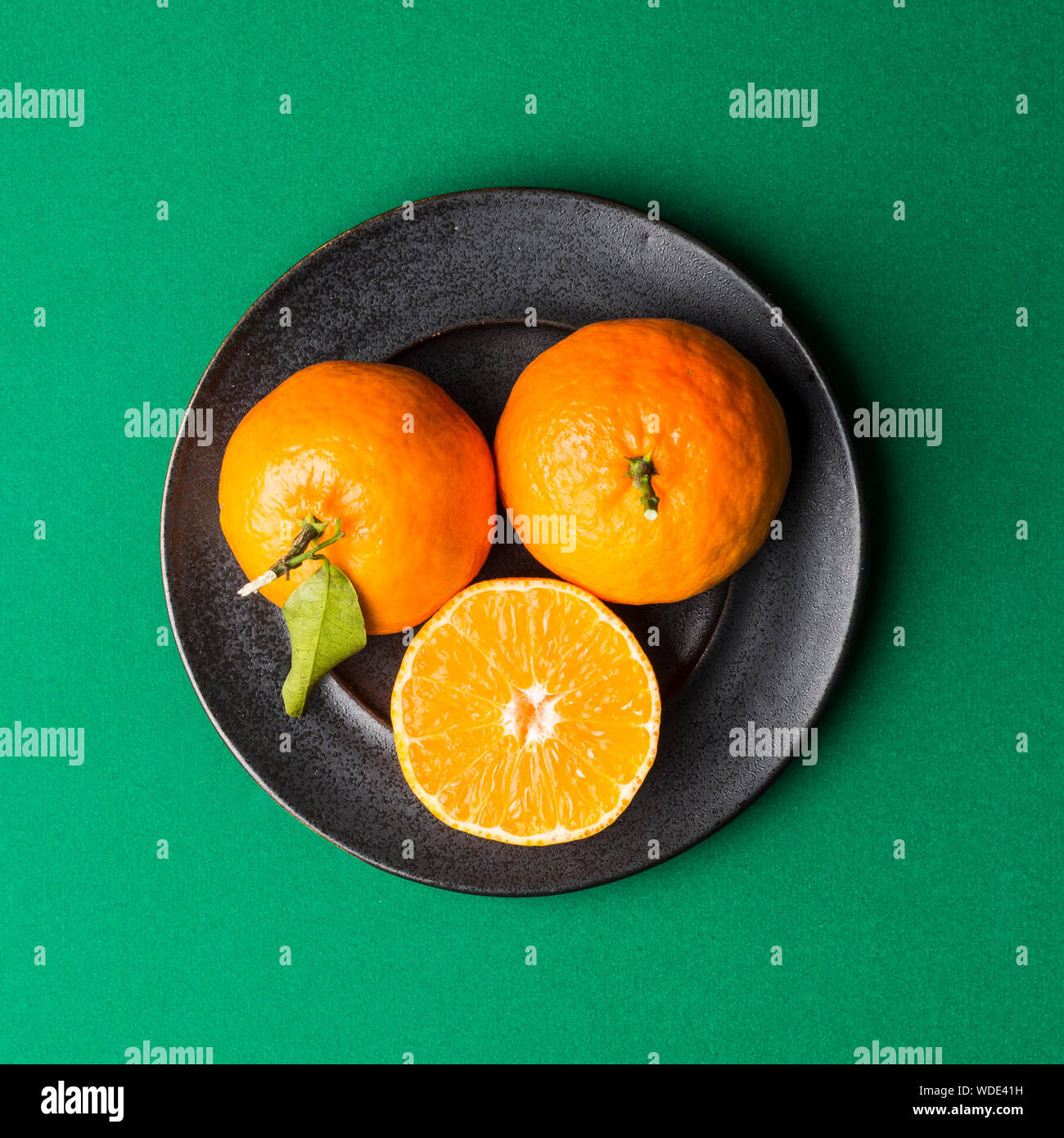 Frondose clementine su rustiche piastra nera, pianura sfondo verde. Foto Stock