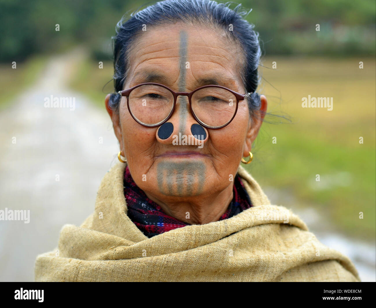 Anziani Apatani indiano donna tribale con legno nero tappi naso (yaping hullo) e distintivo faccia tribale tatuaggio pone per la fotocamera. Foto Stock